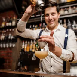 Uśmiechnięty barman przelewa drinka przez sitko. Czy barman może pić w pracy? Ten z pewnością tworzy pyszne koktajle!
