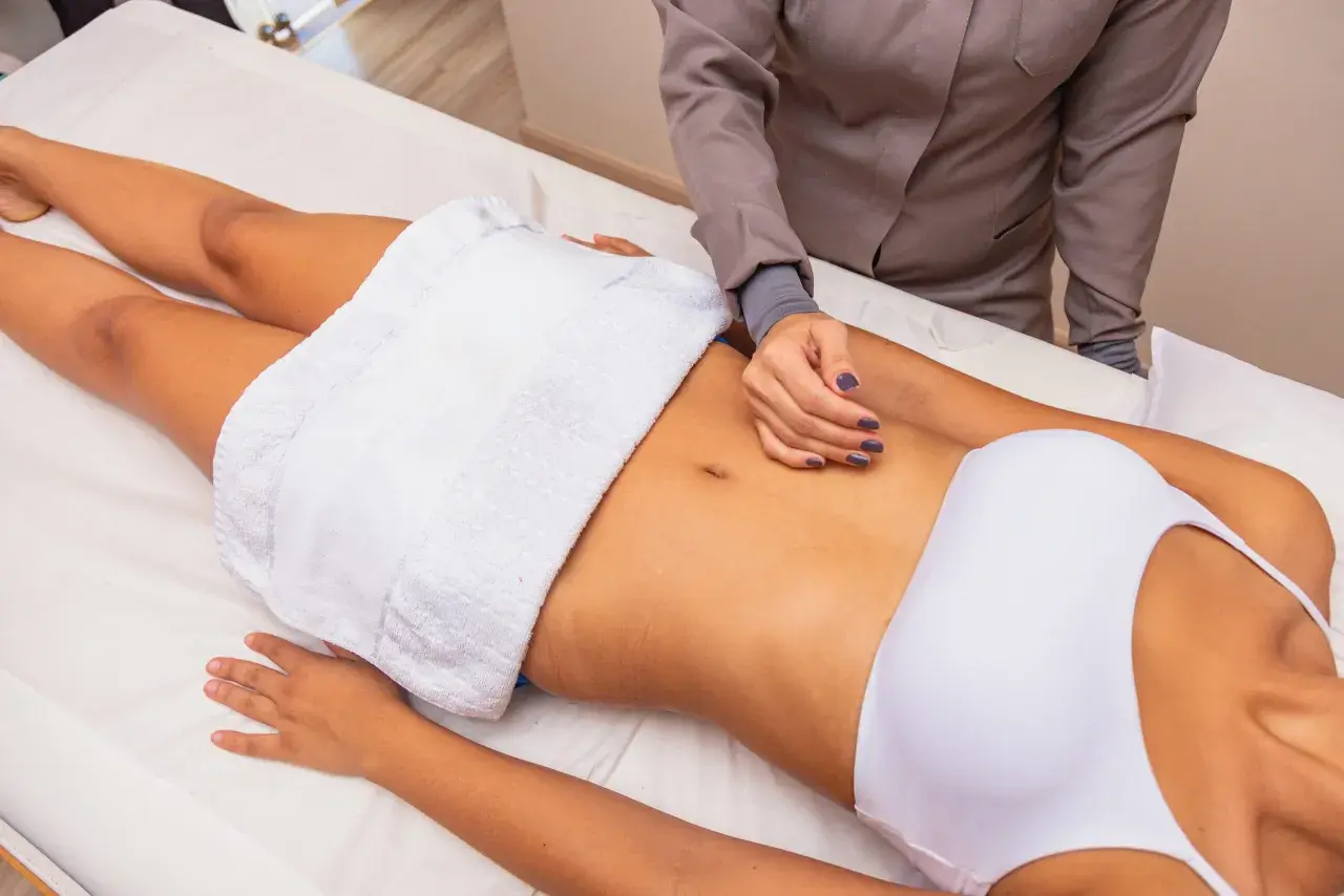 Masaż brzucha jako metoda, jak wyszczuplić brzuch. Terapeuta wykonuje zabieg na leżącej osobie.